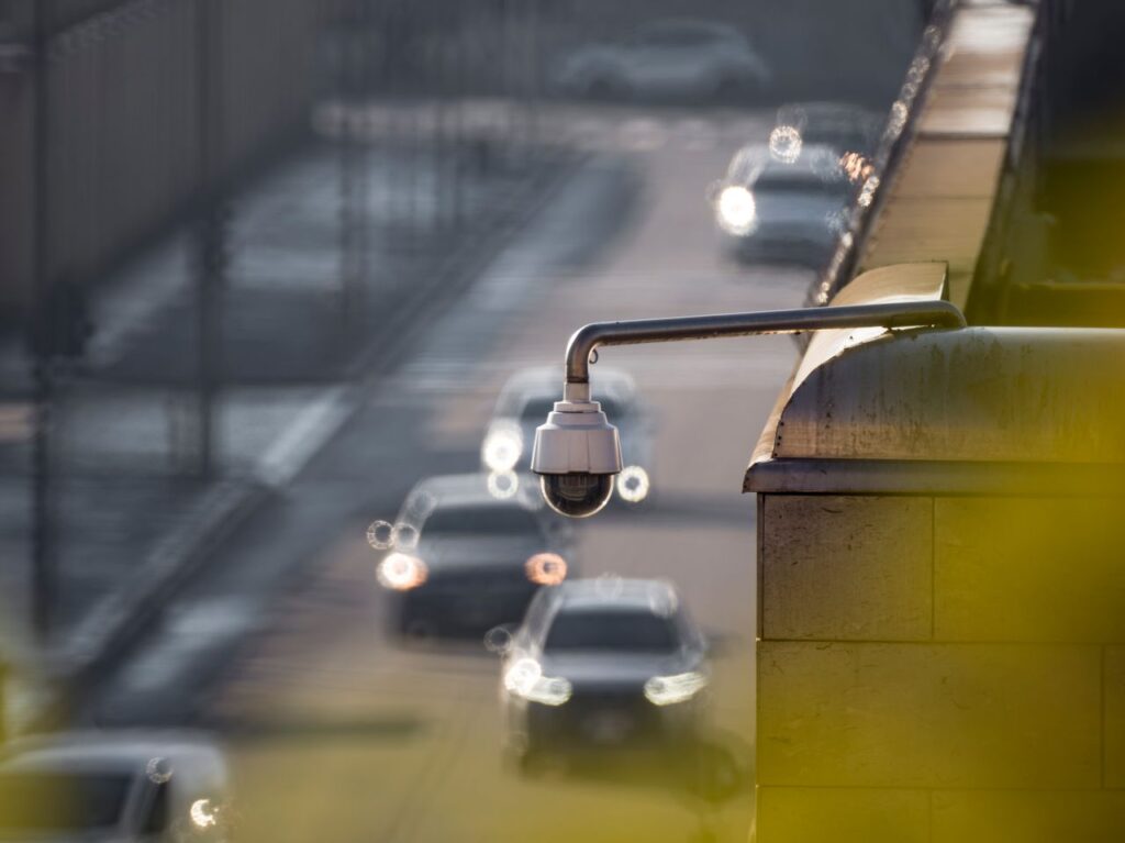 pexels-photo-30546987-30546987 CCTV camera monitoring city traffic on a busy road with blurred vehicles in the background.